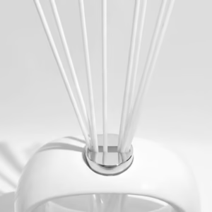 White oval porcelain diffuser vessel with central glass insert and white fibre reeds, styled on a clean surface.