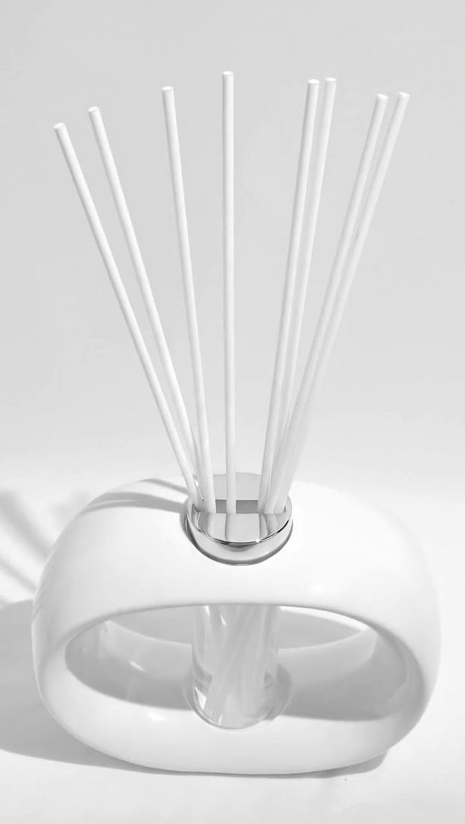 White oval porcelain diffuser vessel with central glass insert and white fibre reeds, styled on a clean surface.
